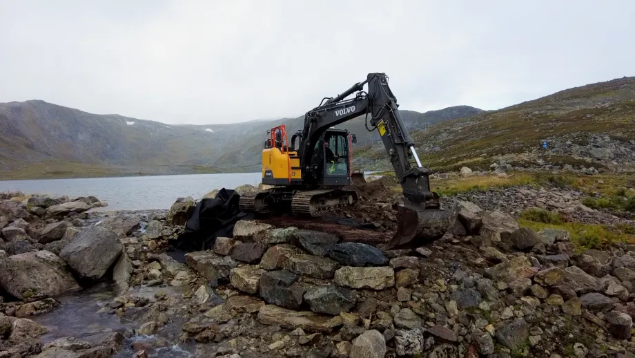 Gravemaskin i arbeid på dammen ved Nedre Svarthammervatnet på Kvaløya.