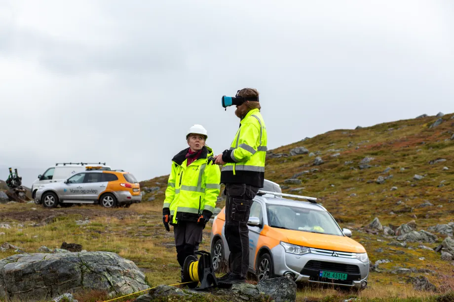 To arbeidere og flere biler på fjellet nært drikkevannskilde.