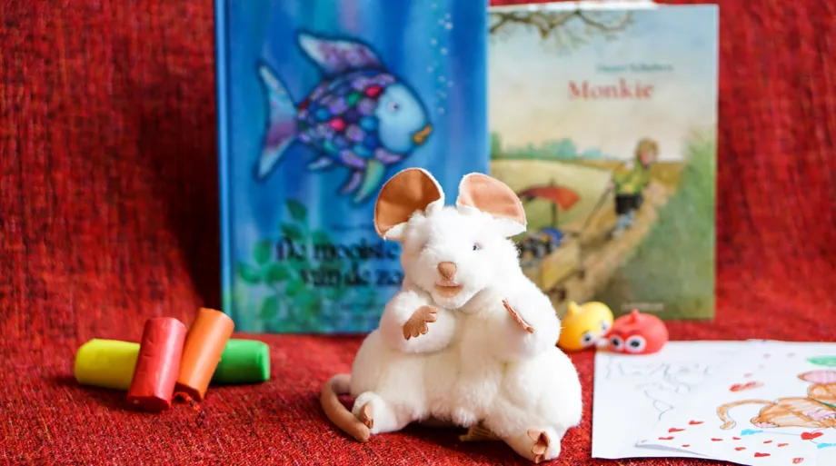 Barnebok, musebamse, tegnestifter og tegneark på rød duk.