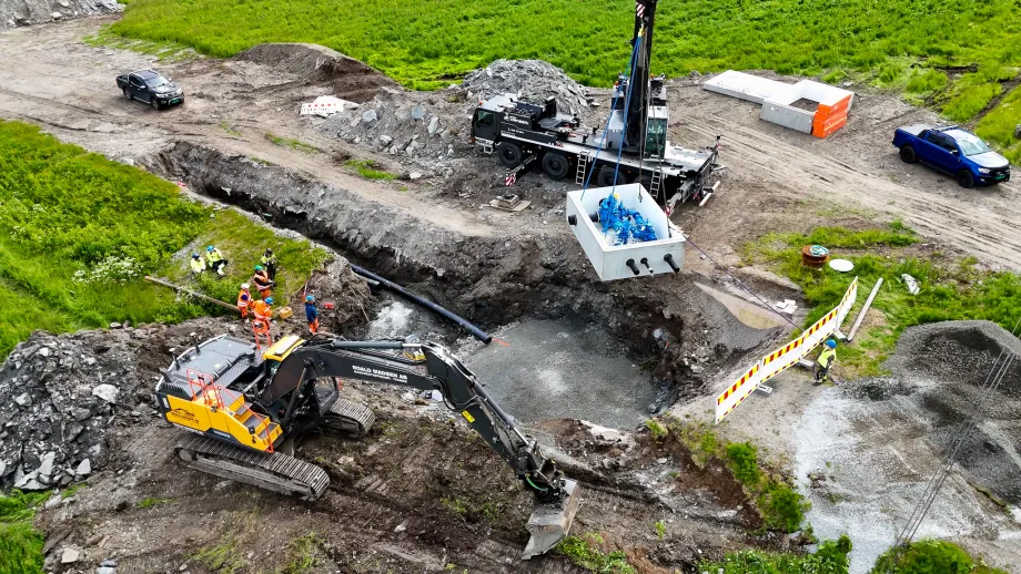 Dronefoto av kum som løftes ned i grøft av heisekran