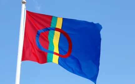 Det samiske flagget p&aring; flaggstang mot bl&aring; himmel. Foto.