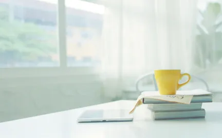 Gul kopp st&aring;r opp&aring; en stabel med b&oslash;ker. Vindu i bakgrunnen. Foto