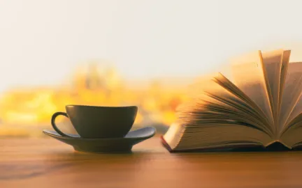 Svart kopp p&aring; svart tefat st&aring;r ved siden av en oppsl&aring;tt bok. Foto.