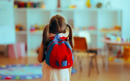 Bilde av liten jente med skolesekk i klasserom