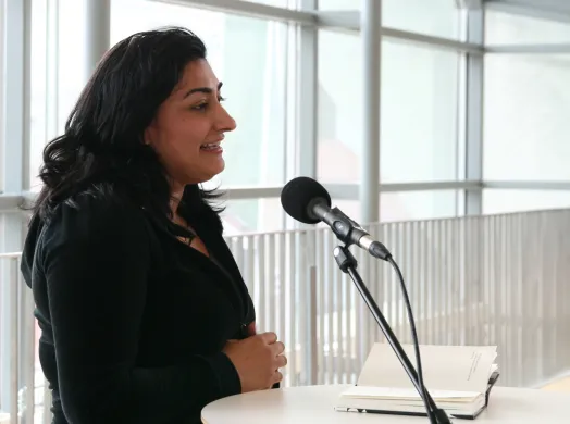 Humor og blodig alvor-Rehman Kvinne med svart hår og svarte klær snakker i en mikrofon. Foto