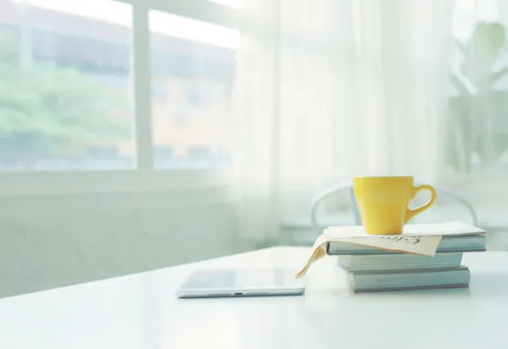 Finn et litterært pusterom 2023 Gul kopp står oppå en stabel med bøker. Vindu i bakgrunnen. Foto