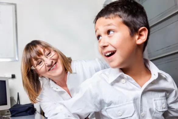 Kvinnelig helsesykepleier sammen med et barn p&aring; et unders&oslash;kelsesrom. Begge smiler til hverandre.