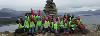 Flere barn med gr&oslash;nne refleksvester fra Karveslettlia barnehage p&aring; tur p&aring; en fjelltopp en gr&aring; h&oslash;stdag
