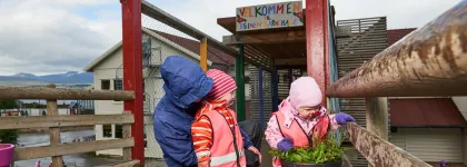 Reinen barnehage inngang med tre barn som ser p&aring; blomster i en krukke en v&aring;t sommerdag
