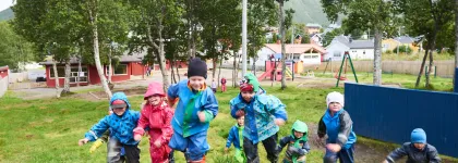 Syv barn som springer opp p&aring; en bakketopp i Tromsdalen barnehage en regntung sommerdag